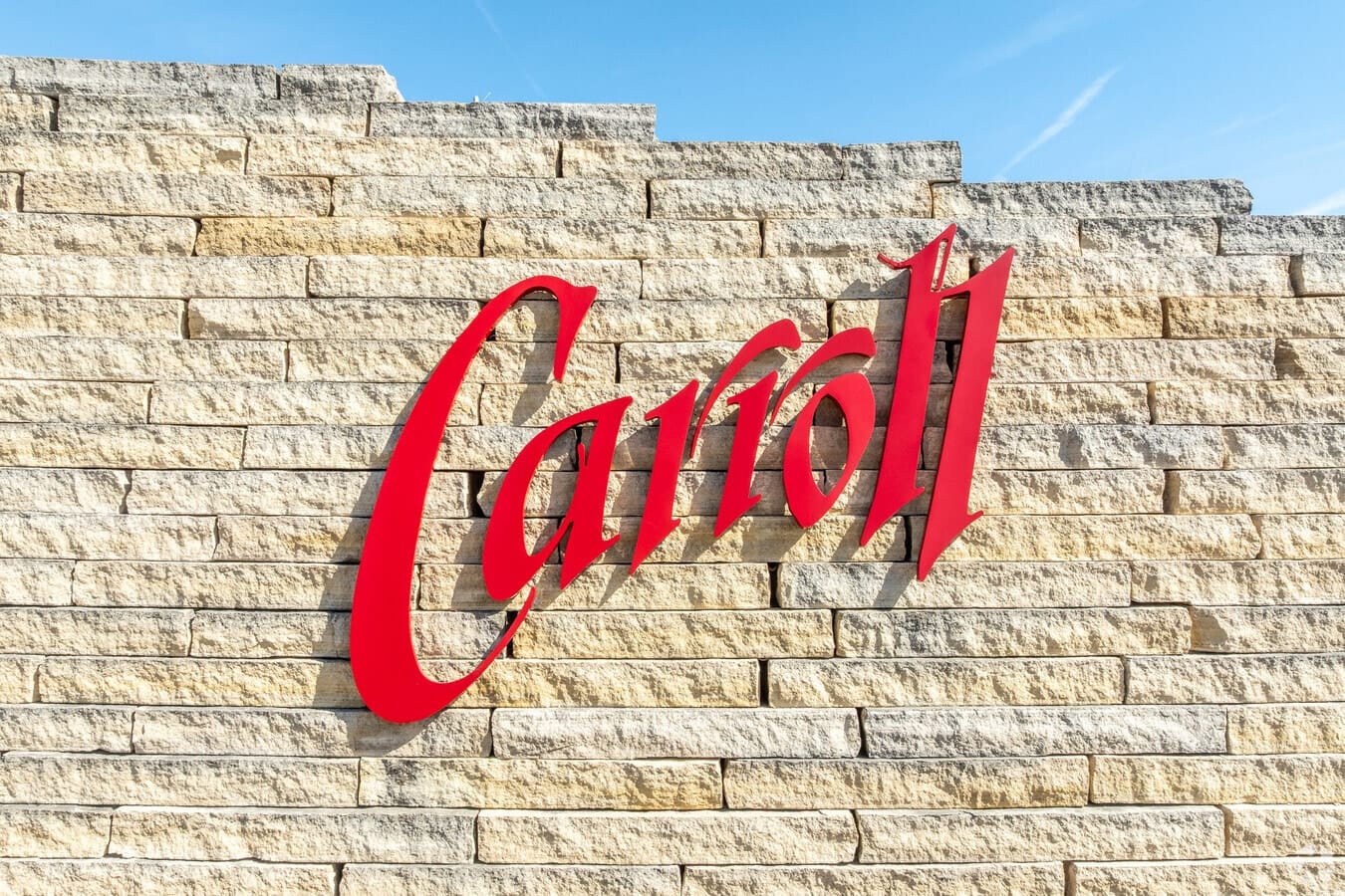 The red script Carroll sign mounted on a stone wall under a blue sky.